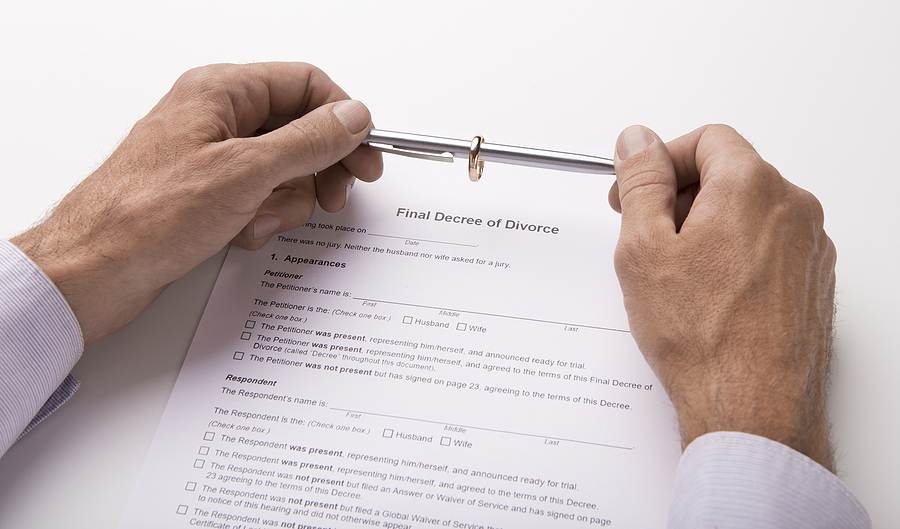 A man holding a pen and his wedding ring together looking on a divorce form